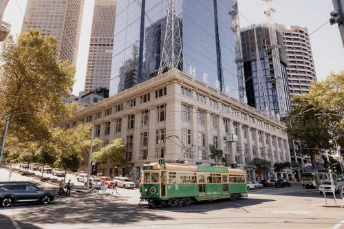 a green trolley driving past a building in a city at A luxe stay in the Paris end of Melbourne in Melbourne