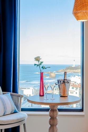 a table with glasses and a window with a view of the ocean at Mercure Président Biarritz Plage in Biarritz