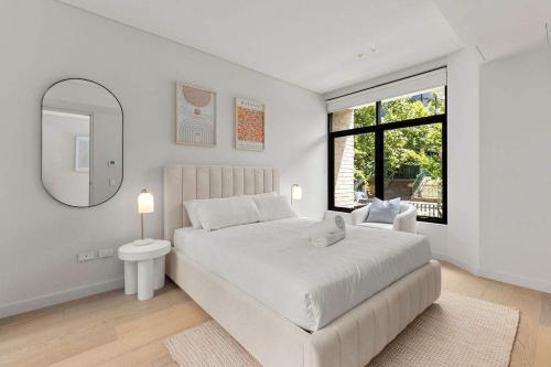 a white bedroom with a large bed and a mirror at Beautiful Holiday Home w Private Terrace in Sydney