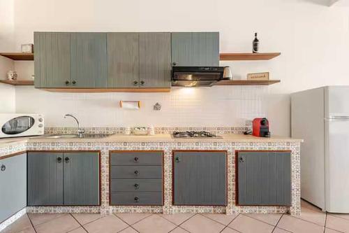a kitchen with gray cabinets and a white refrigerator at Villa Uzzo by Sicily Travelling Villas in Scopello