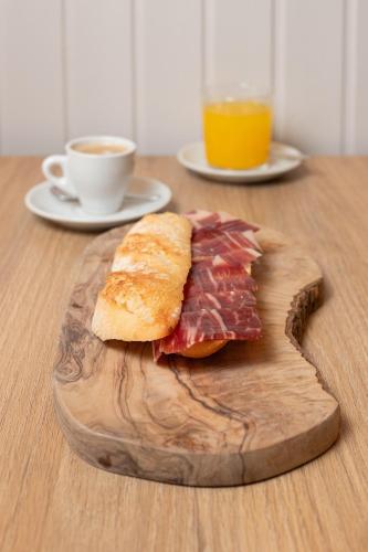 a sandwich on a wooden cutting board with a cup of coffee at HOTEL HACIENDA SANTA BARBARA in Castilleja de la Cuesta