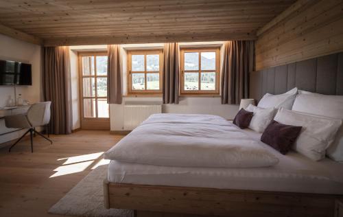 a bedroom with a large white bed and windows at Farm Hotel Chalet Grosslehen in Fieberbrunn