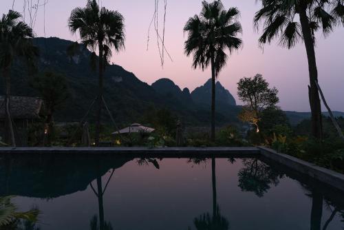 a pool with palm trees and mountains in the background at TOKI Ecolodge Cao Răm in Hòa Bình