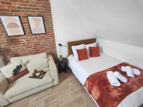 a bedroom with two beds and a couch and a brick wall at Les Briques Rouges, Appartement Béthune in Béthune