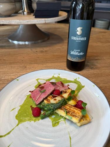 a white plate with food on a table with a bottle of wine at Boutiquehotel DAS ZEITWERT in Deutschlandsberg