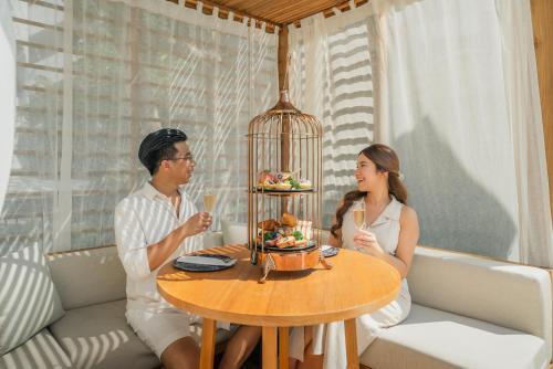 a man and woman sitting at a table with a bird cage at Andaman Beach Hotel Phuket - Handwritten Collection in Patong Beach