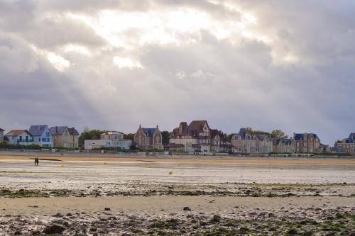 une personne marchant sur une plage avec des maisons en arrière-plan dans l'établissement Maison Cosy à proximité de la Plage, à Hermanville-sur-Mer