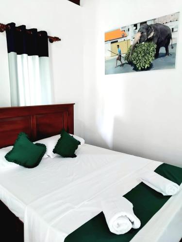 a white bed with green pillows and a picture of an elephant at Seeing Green Udawalawa in Udawalawe