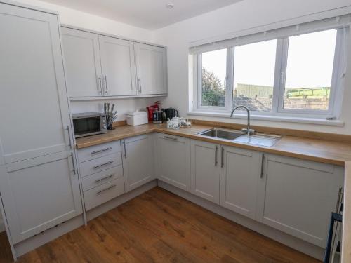a kitchen with white cabinets and a sink and two windows at Arfryn in Haverfordwest
