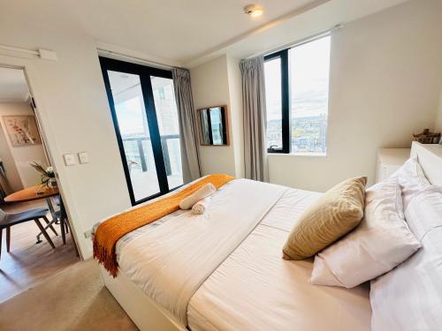 a bedroom with a large white bed with windows at Sky Tower Panorama Suite Luxurious Apartment in Auckland