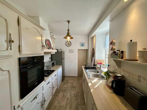 une grande cuisine avec des placards blancs et un évier dans l'établissement Pretty charming Breton cottage for 4 people, à Trédrez
