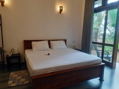a bedroom with a bed with white sheets and a window at Turtle Point Homestay in Batigama