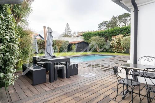 une terrasse avec une piscine, une table et un parasol dans l'établissement Villa Augusta – Biarritz Phare, à Anglet