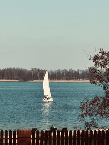 a sailboat in the water with a person on a fence at Świat Jezior in Mikołajki