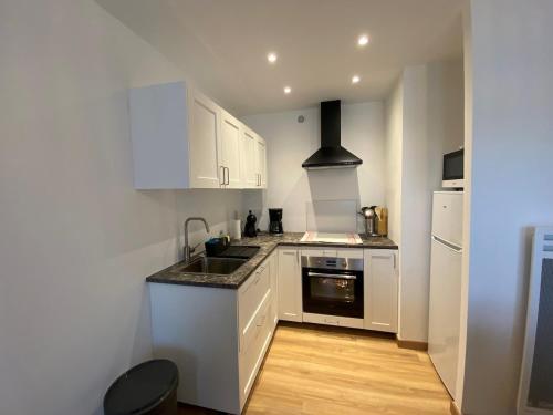 une cuisine avec des armoires blanches, un évier et une cuisinière dans l'établissement Charmant appartement résidence Haute Mer, à Fort-Mahon-Plage