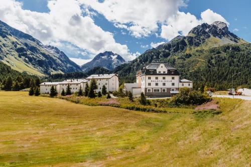 a large building in a field with mountains in the background at Hotel Maloja Kulm in Maloja