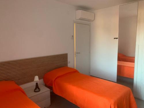 two beds in a bedroom with orange sheets at Luciano Home in Gonnesa
