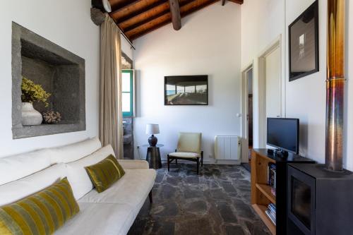 a living room with a white couch and a tv at Pico do Refúgio - Casas de Campo in Ribeira Grande
