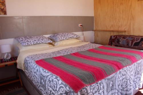 a bed with a red and white blanket on it at Cabaña Nachitor in San Pedro de Atacama