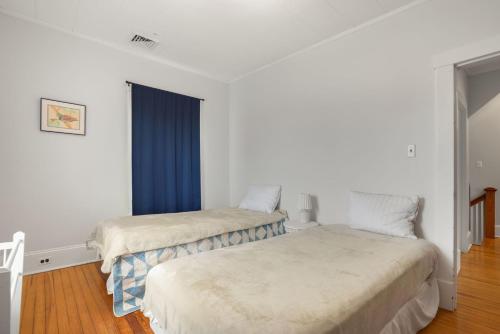 two beds in a room with white walls and blue curtains at Maison des Reves - Historic charm in the heart of Downtown! in Cape Charles