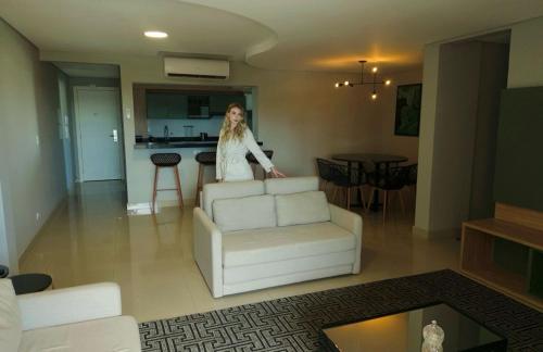 a woman standing in a living room with a white couch at ApartDamani - Aptos por Temporada no centro in Foz do Iguaçu