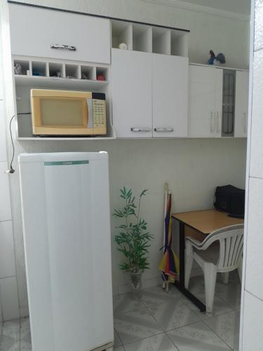 a kitchen with white cabinets and a table with a microwave at Aconchego in Praia Grande