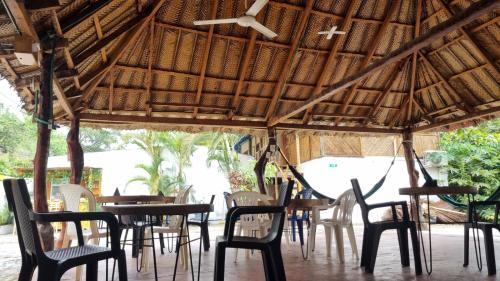 a group of tables and chairs under a straw roof at Las Cascadas Hostel in Buritaca