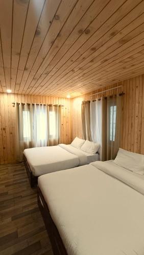 three beds in a room with wooden walls and windows at Hotel Himalayan in Madheso