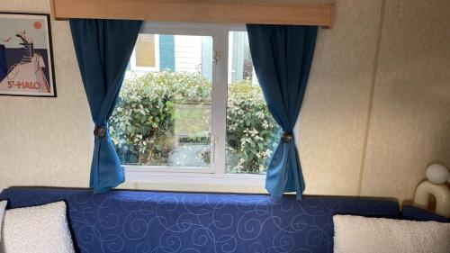 une fenêtre avec des rideaux bleus et un canapé bleu dans l'établissement Mobil-Home le 70 du White Port, à Dinard