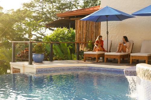 two women sitting under an umbrella next to a swimming pool at Casa Marbella in Santa Teresa Beach