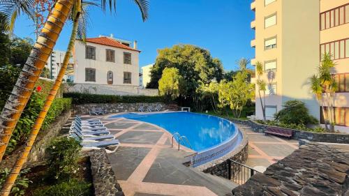 a swimming pool next to a building and a palm tree at Apto Barreiro by Susy's Holidays in Funchal