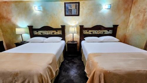 two beds in a hotel room with two lamps at Antigua Inn Hotel in Guatemala