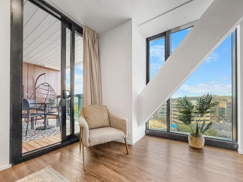 a living room with a chair and large windows at Ellerslie Sanctuary- Modern, quality apartment in Auckland