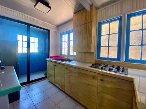 a kitchen with wooden cabinets and blue windows at Hostal Casa La Puntilla in Los Molles