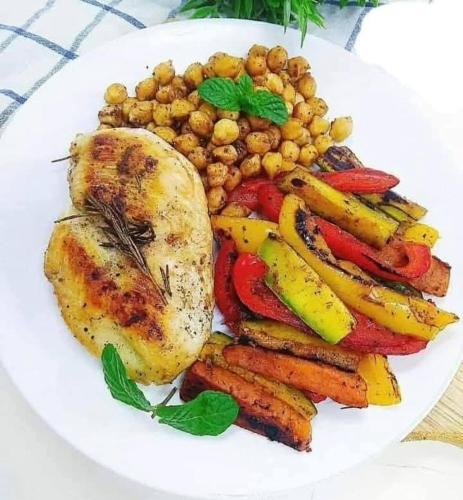 a plate of food with chicken and vegetables on a table at 77 apartment in Abū aş Şalīḩ