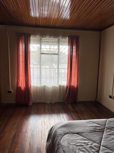 a bedroom with a bed and a window with red curtains at El Garaje b&b in Zarcero