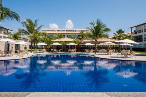 a large swimming pool with palm trees and umbrellas at GUARAJUBA Condomínio PARAÍSO DOS CORAIS BEACH RESORT 132 in Guarajuba