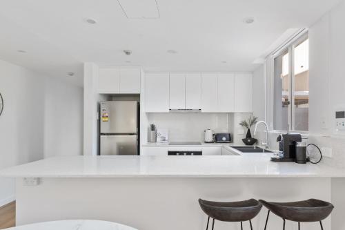 a white kitchen with white cabinets and two stools at Stylish 2-Bed Apartment with Pool in Camperdown in Sydney