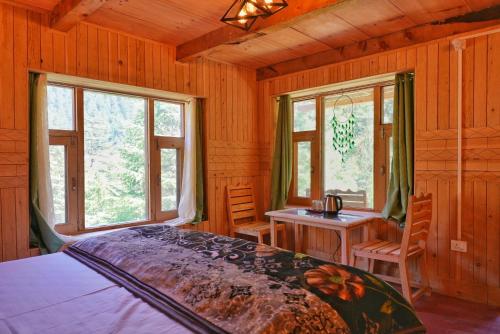 a bedroom with a bed and a desk and windows at Ailyak Stays Seri in Jibhi