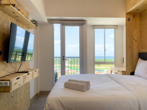 Un dormitorio con una cama y un televisor y ventanas. en Minimalist Studio Room at Tokyo Riverside PIK 2 Apartment By Travelio, en Rawalembang