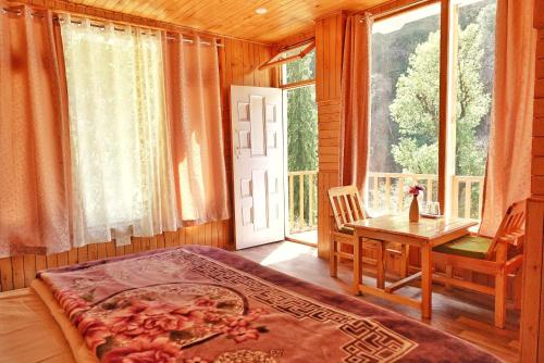 a bedroom with a bed and a table and a window at Ailyak Stays and Cafe, Shoja, Jibhi in Shoja