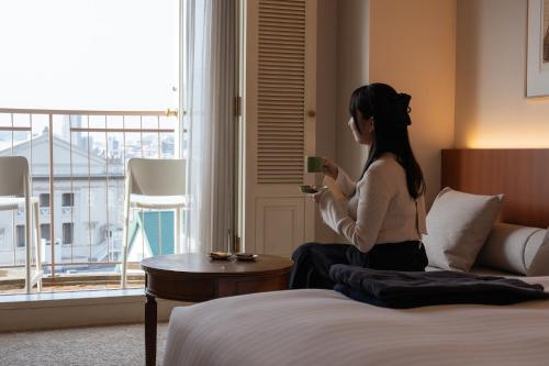 a woman sitting on a bed looking at her cell phone at Setre Glover's House Nagasaki in Nagasaki