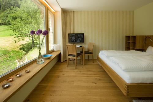 a bedroom with a bed and a table and a window at Hotel Alpenrose Ebnit in Dornbirn