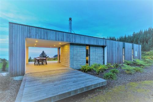a house with a wooden deck and a table at Ligar Escape - Golden Bay Holiday Home in Tarakohe