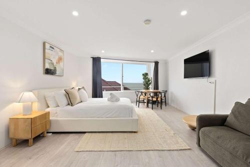 a white bedroom with a large bed and a table at Iconic Bondi Beach Views in Sydney