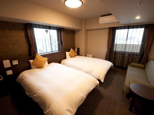 two beds in a hotel room with two windows at Dormy Inn Premium Namba Natural Hot Spring in Osaka