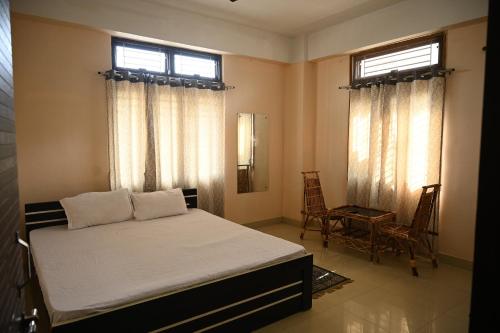 a bedroom with a bed and a chair and two windows at Rising Homestay in Guwahati
