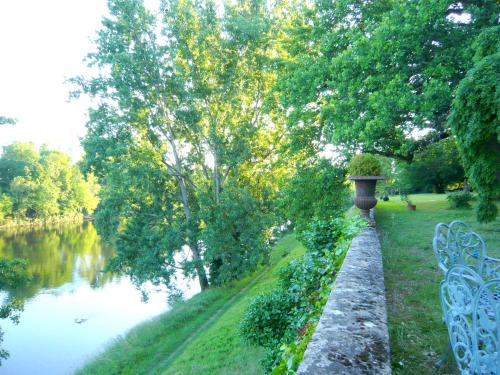 a park bench next to a river with a tree at La Rebière d'Or, B&B et Gîte in Mouleydier