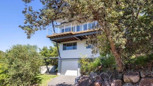 a white house with a balcony and a tree at Hamptons By The Bay in Nelson Bay