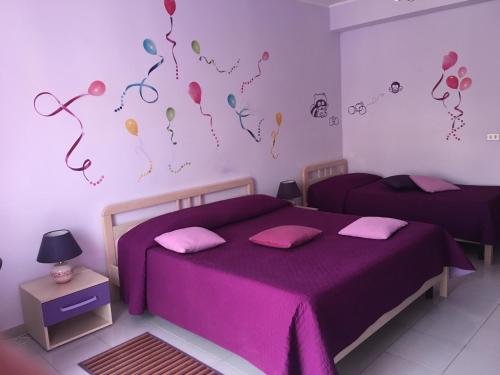 1 dormitorio con 2 camas con sábanas moradas y globos en la pared en I Colori dell'Arcobaleno, en Santo Stefano di Camastra